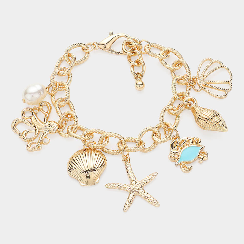 Gold bracelet with sea creature charms and pearl on white stone background