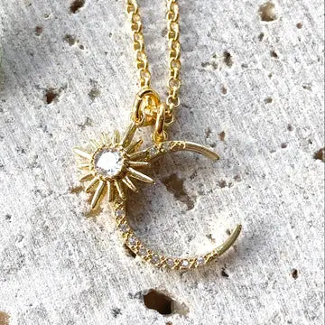 Gold moon and sun charm necklace with crystal accents on neutral background